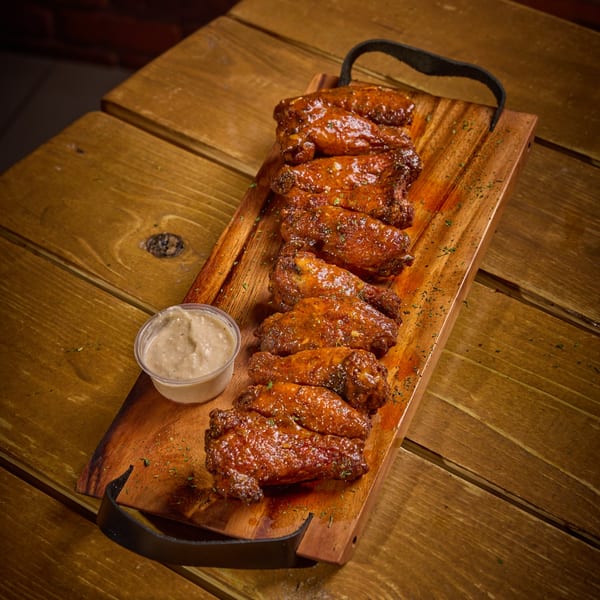 Glazed chicken wings with herbs and a side of dipping sauce on a wooden serving board.