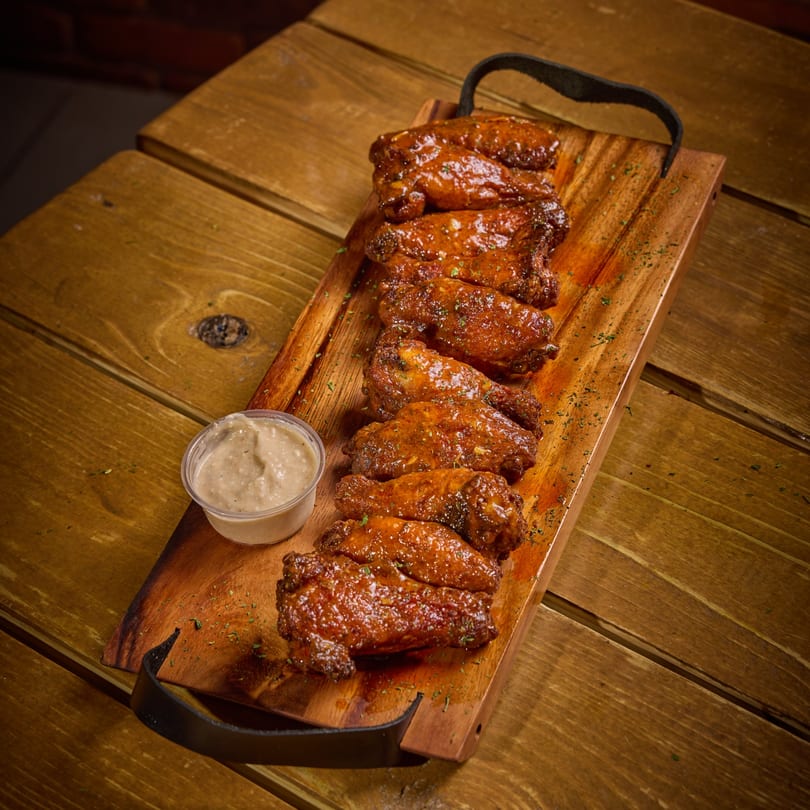 Glazed chicken wings with herbs and a side of dipping sauce on a wooden serving board.