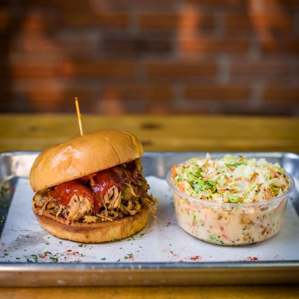 Pulled pork sandwich with barbecue sauce and a side of coleslaw on a metal tray.