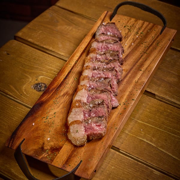 Sliced steak with coarse salt and herbs on a wooden serving board.
