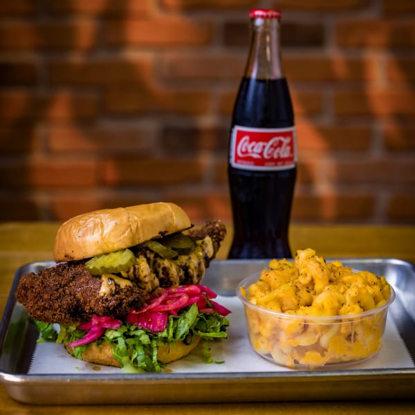 Crispy chicken sandwich with pickles, lettuce, and red onions, with mac and cheese and a Coke.