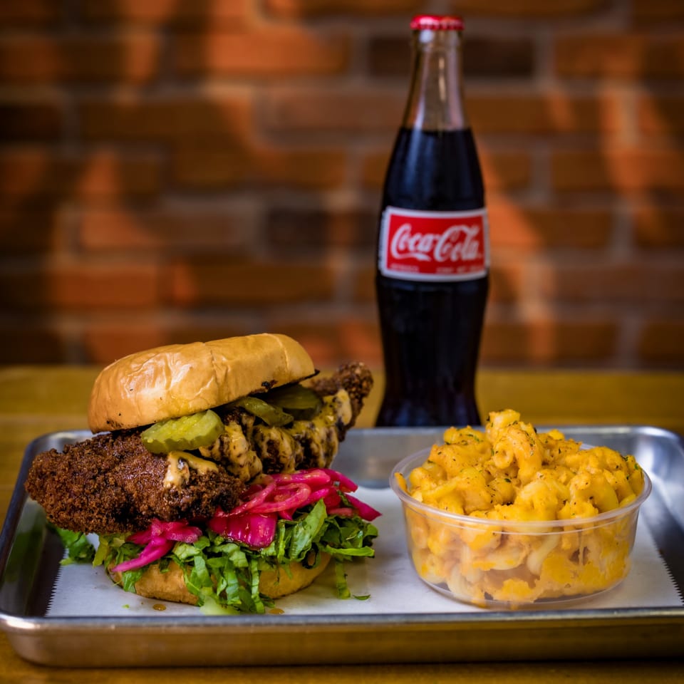 Crispy chicken sandwich with pickles, lettuce, and red onions, with mac and cheese and a Coke.