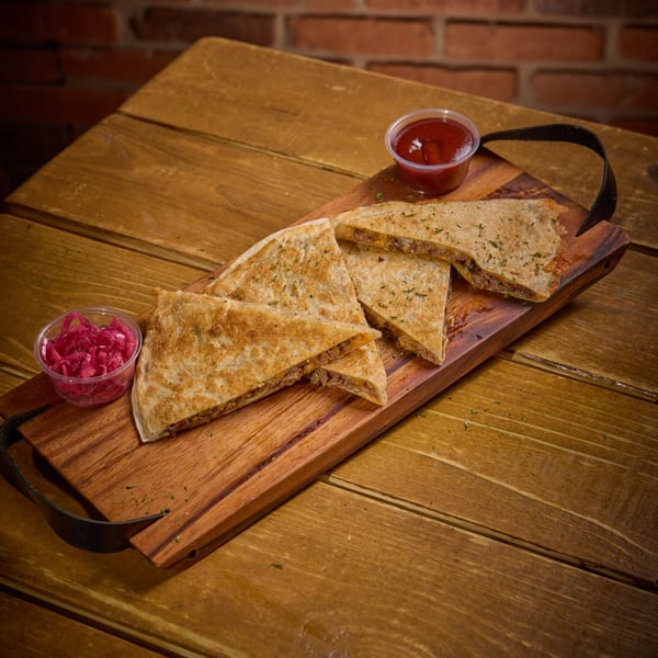 Quesadilla slices with meat filling, served on a wooden board with red sauce and pickled onions.