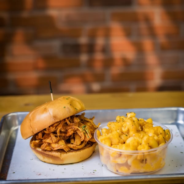 Pulled pork sandwich with a side of macaroni and cheese on a metal tray.