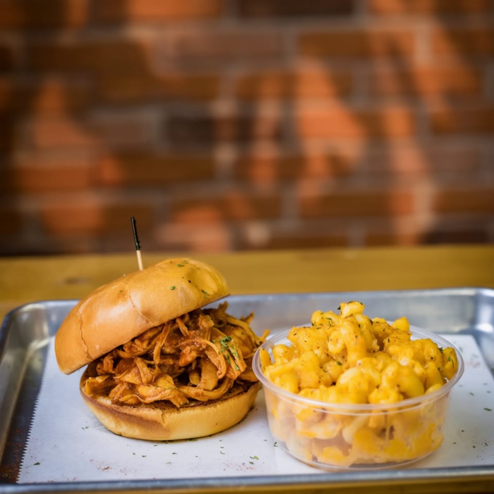 Pulled pork sandwich with a side of macaroni and cheese on a metal tray.